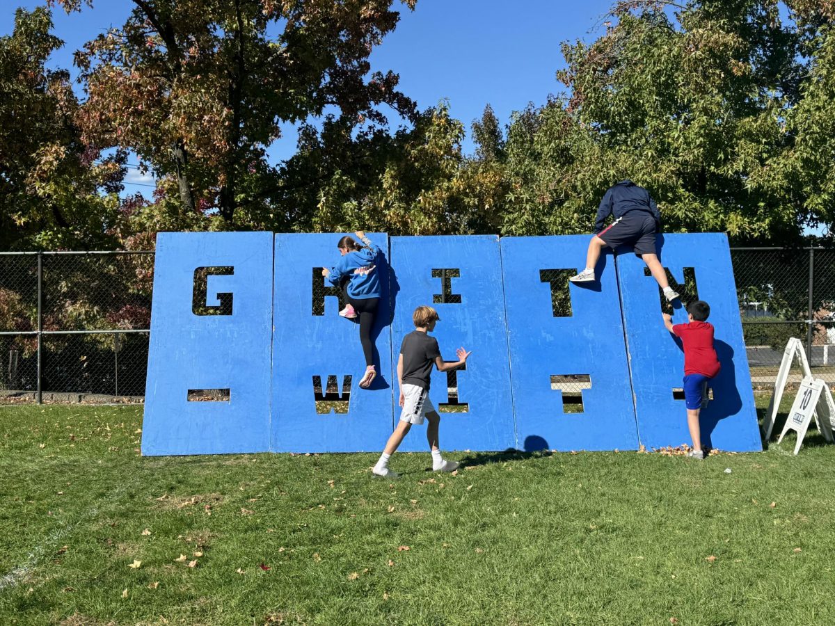 Students climbing across a wall spelling out GRIT N WIT.